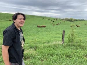Student stands in front of pastured cattle